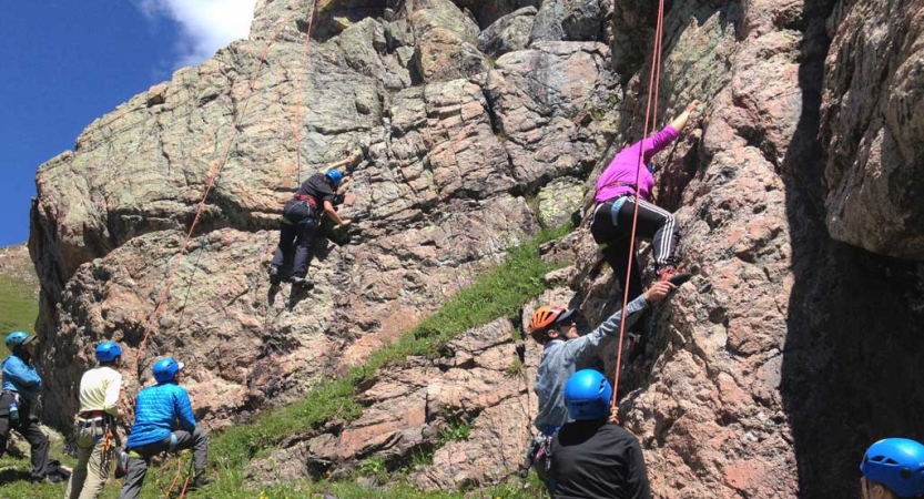 A group of people wearing safety gear climb and belay at a rock wall 